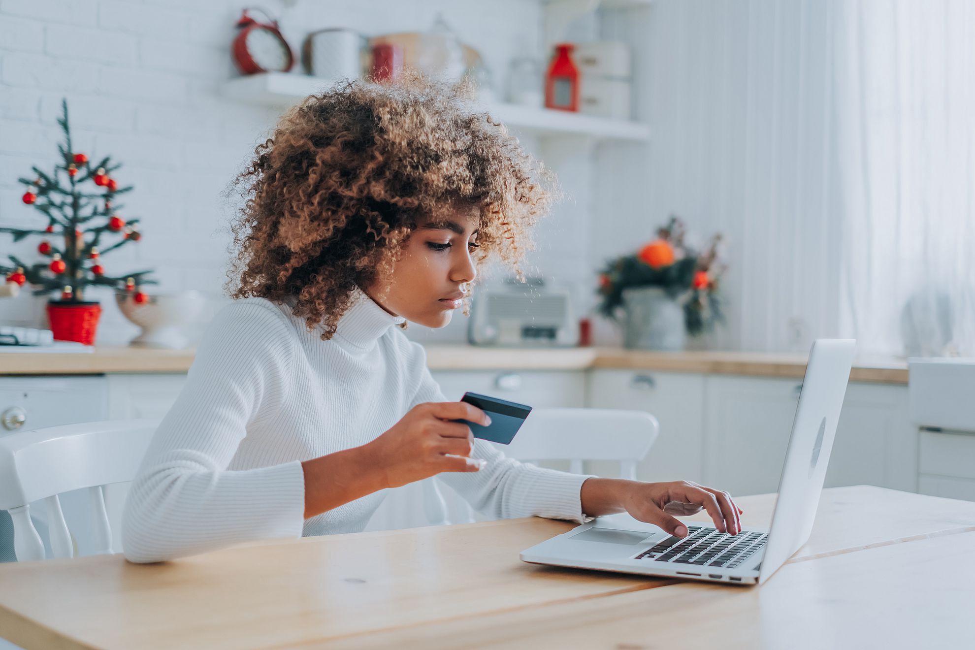 Mulher sentada em uma cadeira, segurando um cartão, mexendo no computador a mesa, vendo sua fatura Credz